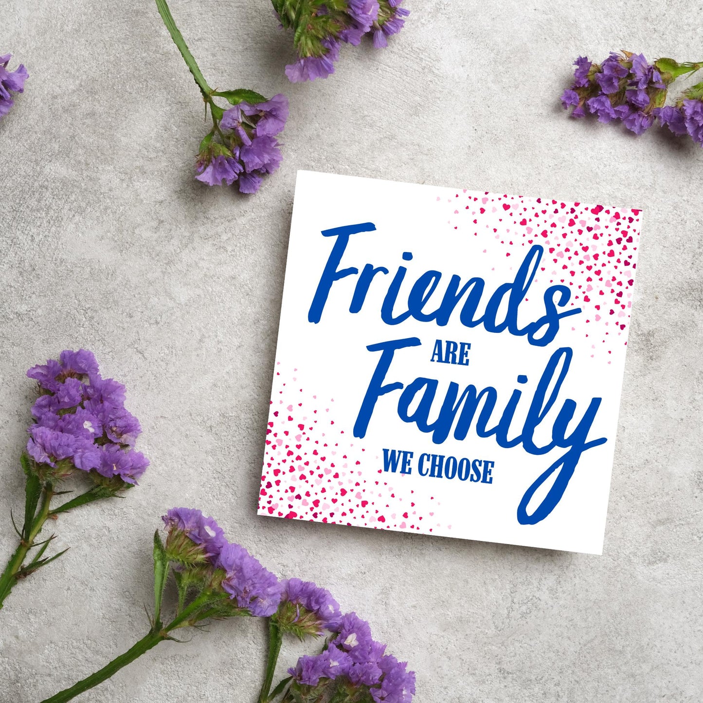 Square card with small hearts on opposite corners in shades of pink and blue writing in the centre that reads Friends are Family we choose