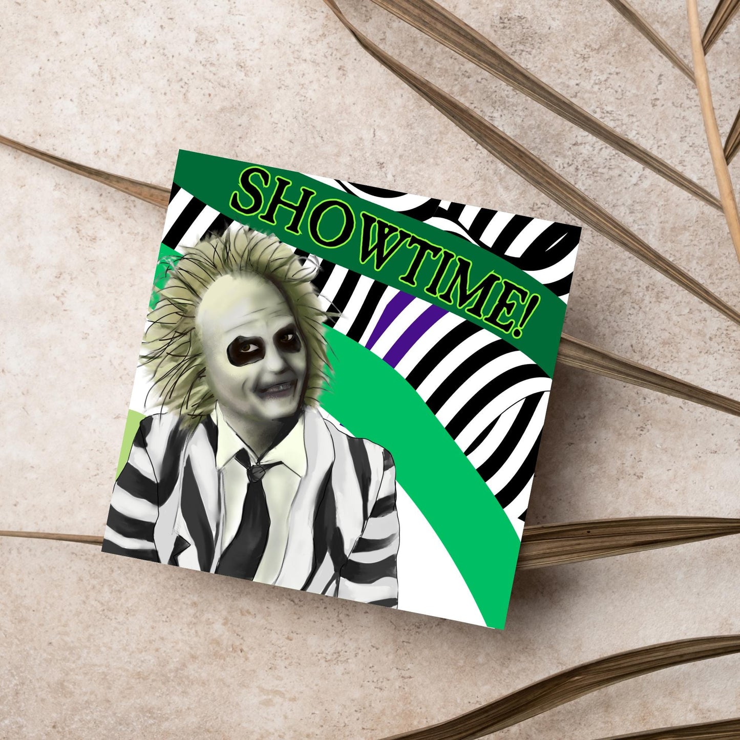 square greeting card with a drawn image of beetlejuice grinning in from of a black, green and purple striped background. On one of the biggest stripes is the word showtime in bold capital letters in a font similar to the movie title