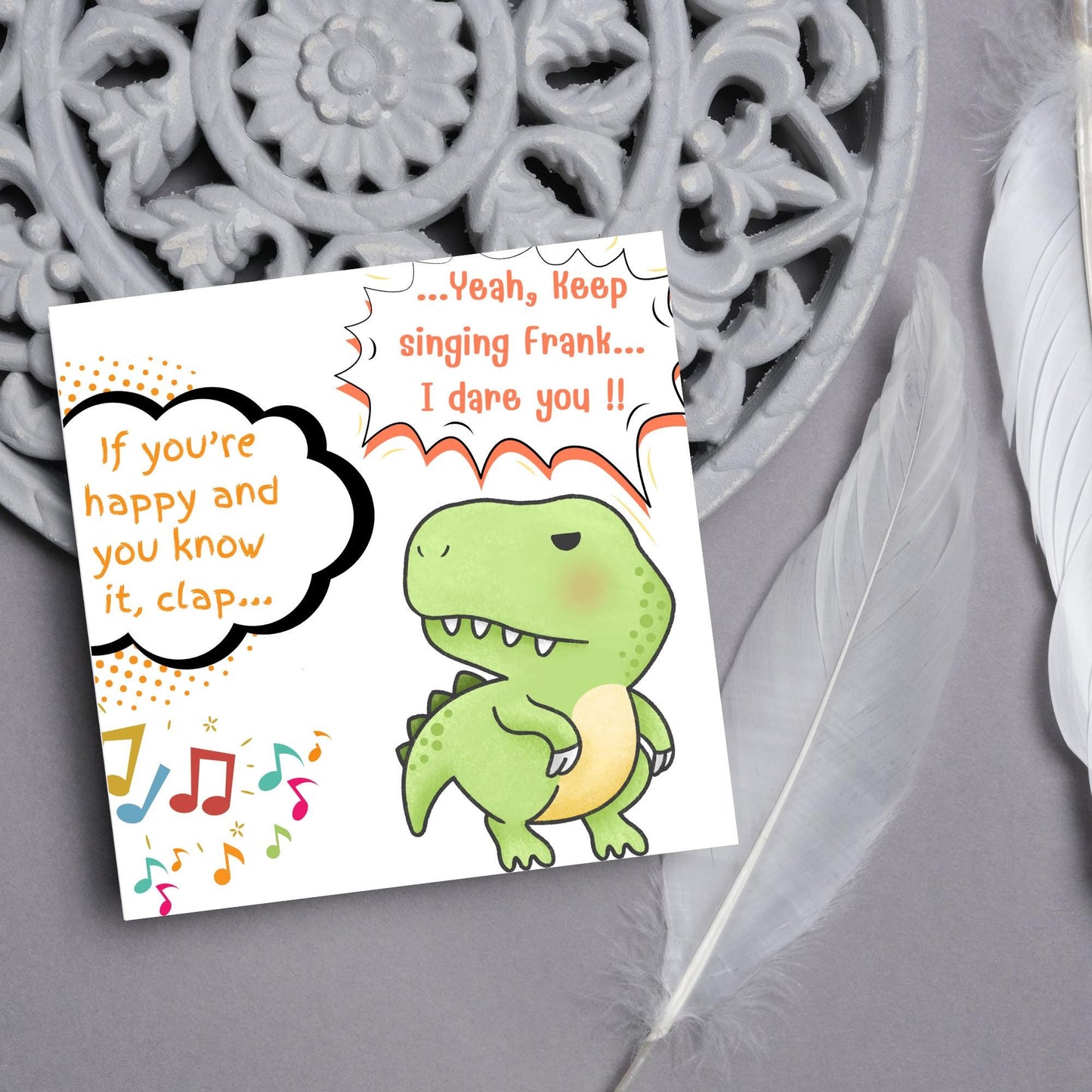 A cute, grumpy green T-Rex with tiny arms is featured. Text reads, "If you're happy and you know it, clap..." The T-Rex responds, "...Yeah, keep singing Frank... I dare you!!" Musical notes add a playful touch.