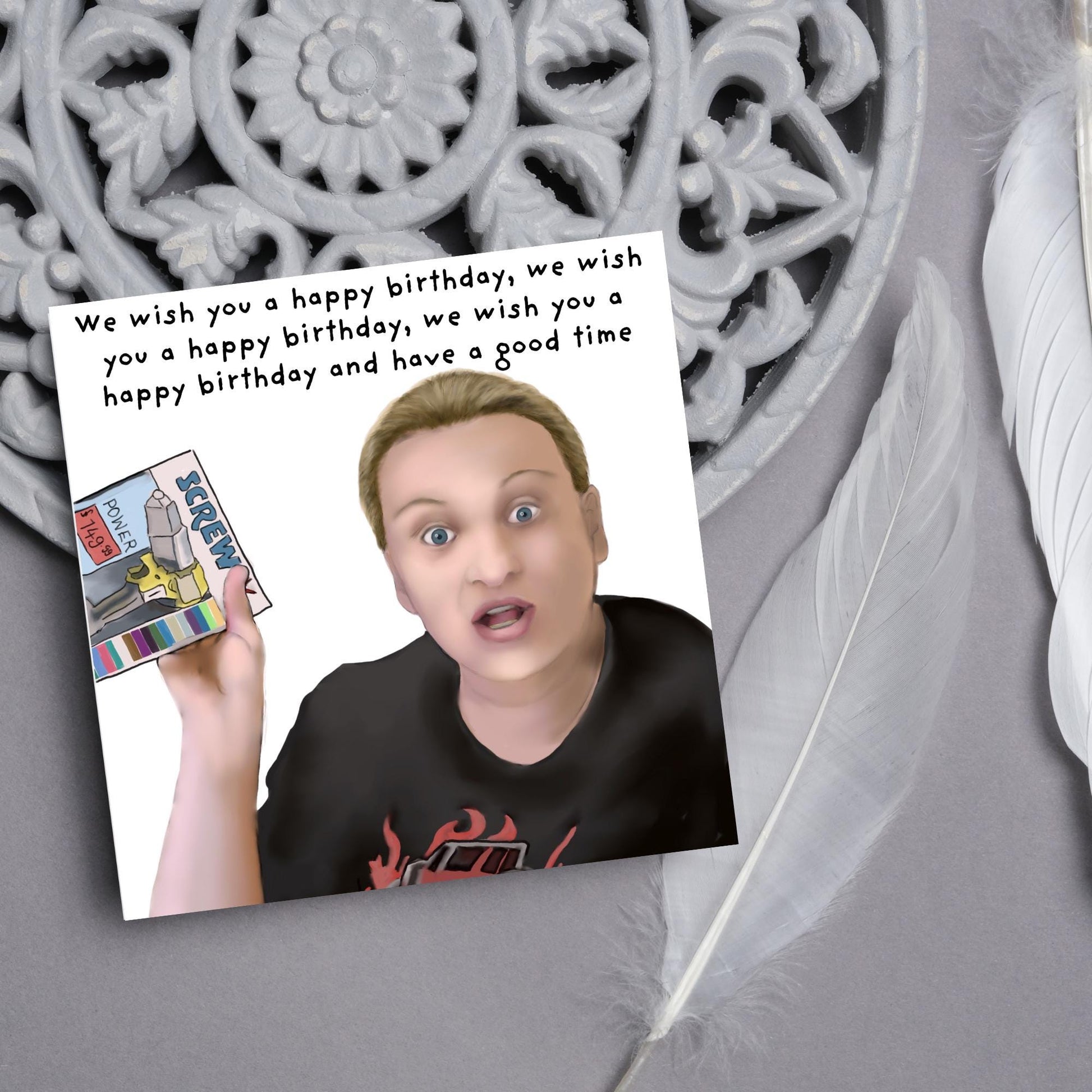 Square birthday card with a hand drawn image of Kerry from this country looking shocked and holding up a screwfix catalogue with the text we wish you a happy birthday, we wish you a happy birthday, we wish you a happy birthday and have a good time