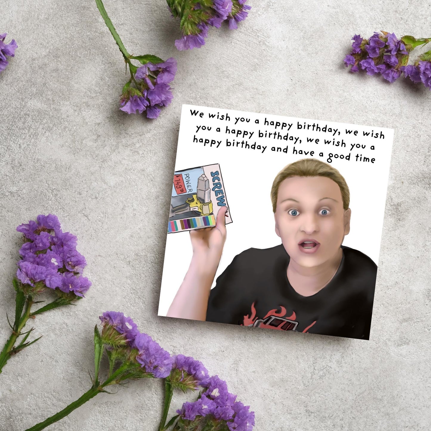 Square birthday card with a hand drawn image of Kerry from this country looking shocked and holding up a screwfix catalogue with the text we wish you a happy birthday, we wish you a happy birthday, we wish you a happy birthday and have a good time