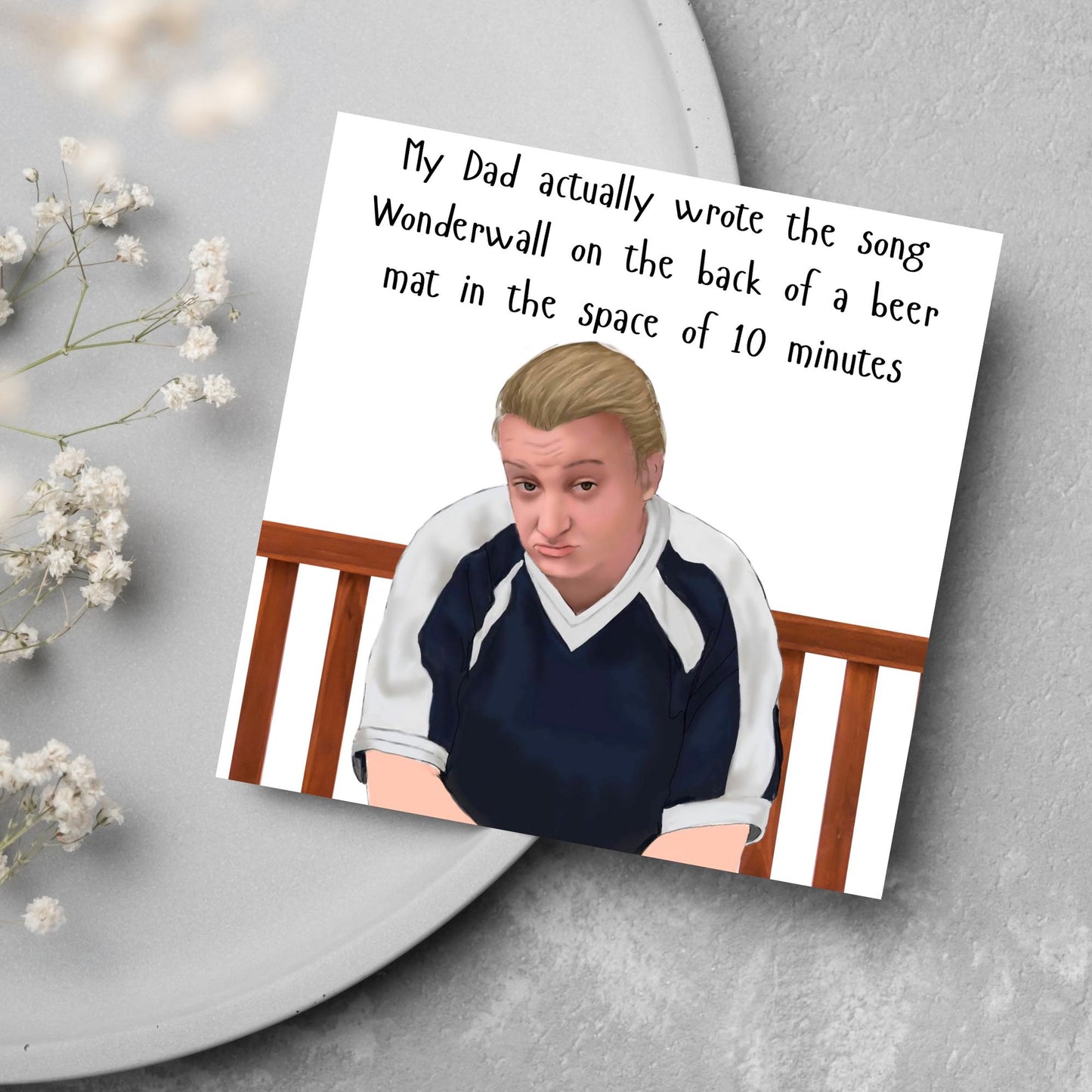 square card with a hand drawn image of kerry from this country sitting on a bench with handwritten style text above - My Dad actually wrote the song Wonderwall on the back of a beer mat in the space of 10 minutes