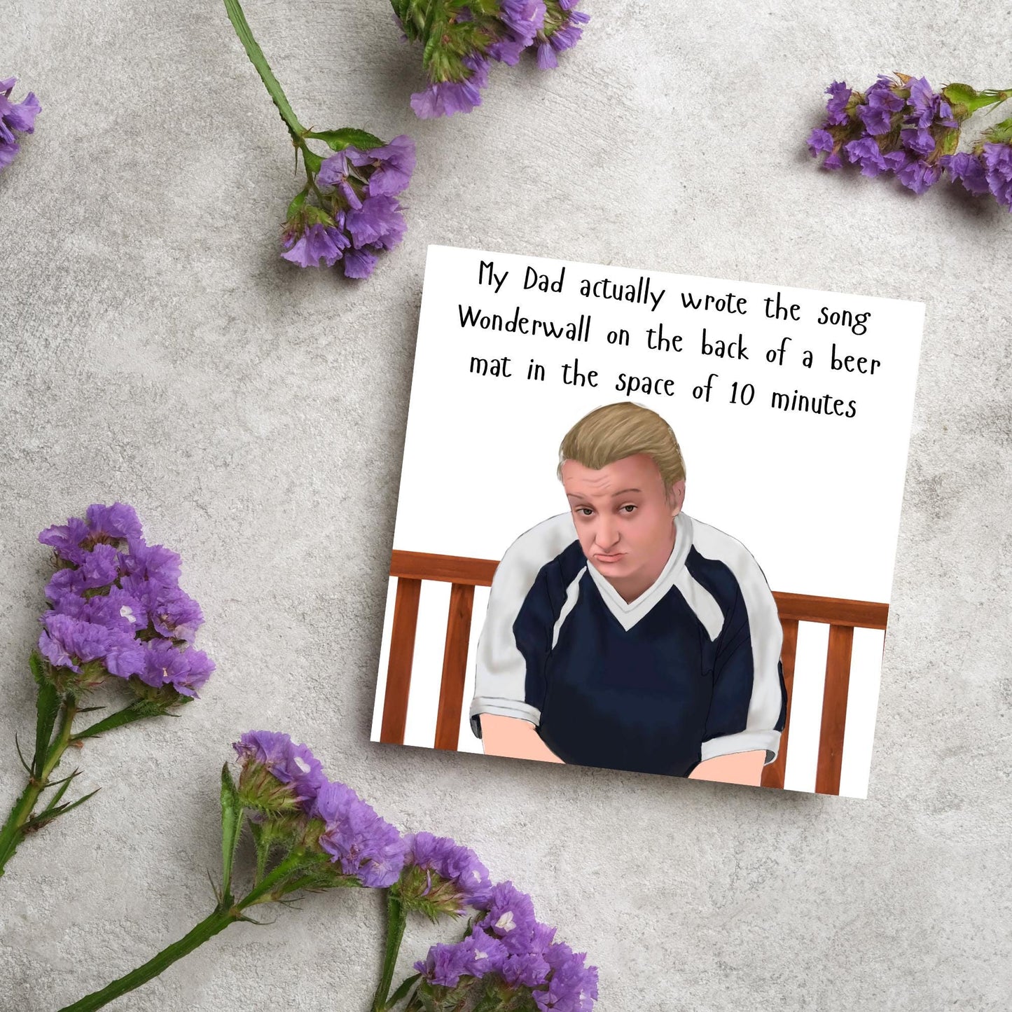 square card with a hand drawn image of kerry from this country sitting on a bench with handwritten style text above - My Dad actually wrote the song Wonderwall on the back of a beer mat in the space of 10 minutes
