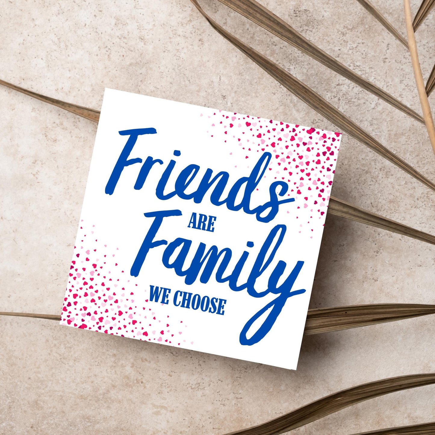 Square card with small hearts on opposite corners in shades of pink and blue writing in the centre that reads Friends are Family we choose