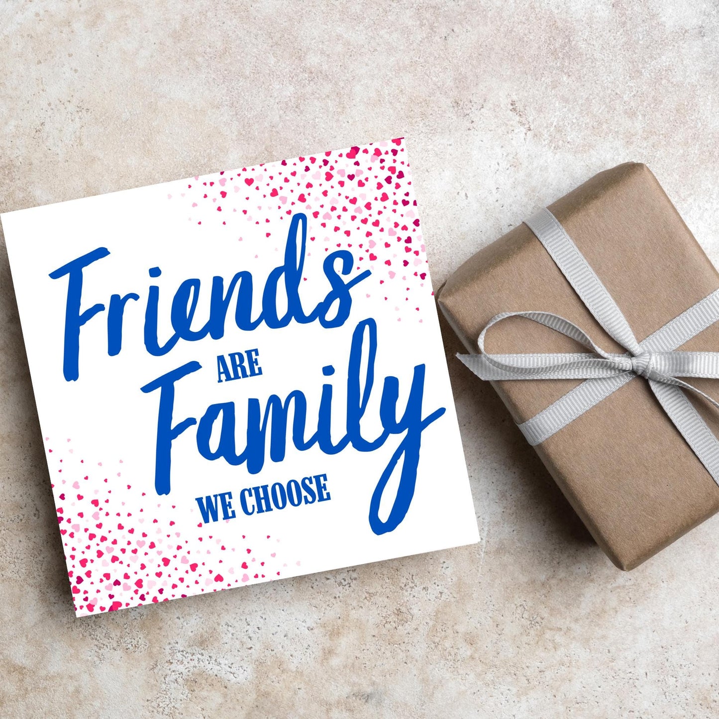Square card with small hearts on opposite corners in shades of pink and blue writing in the centre that reads Friends are Family we choose