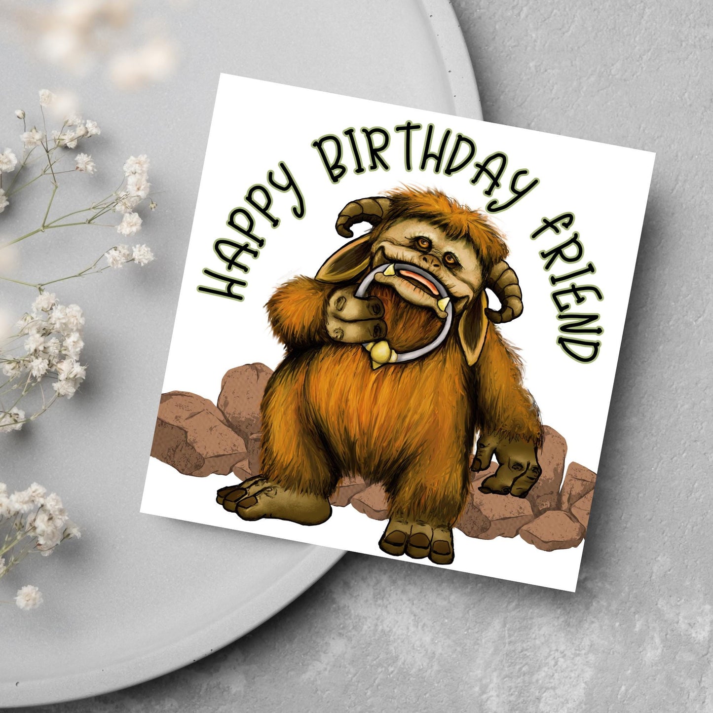 This square shaped card has an illustration of Ludo from the 80s Bowie film Labyrinth. Ludo towers over some rocks and has a door knocker in their mouth. The caption reads Happy Birthday Friend, this text arches above Ludo. This card is perfect for any fans of the film Labyrinth