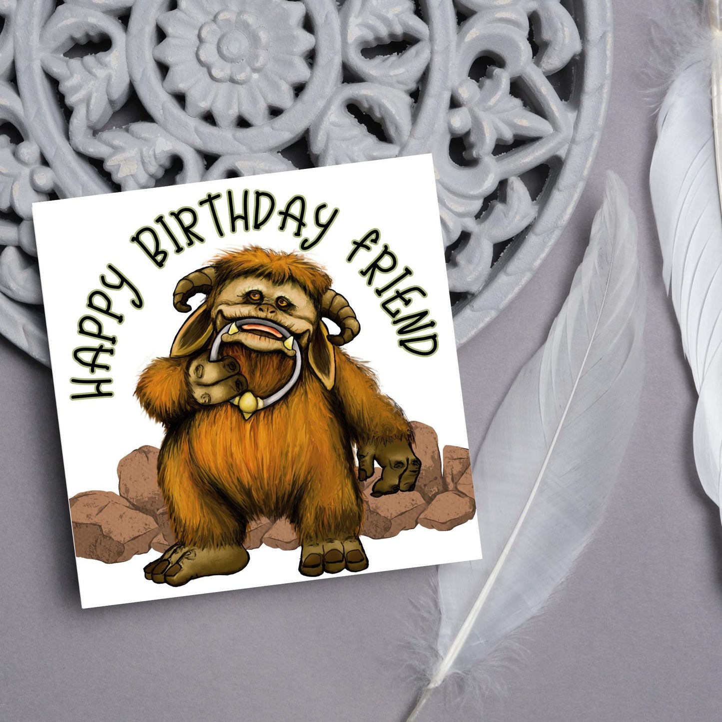 This square shaped card has an illustration of Ludo from the 80s Bowie film Labyrinth. Ludo towers over some rocks and has a door knocker in their mouth. The caption reads Happy Birthday Friend, this text arches above Ludo. This card is perfect for any fans of the film Labyrinth