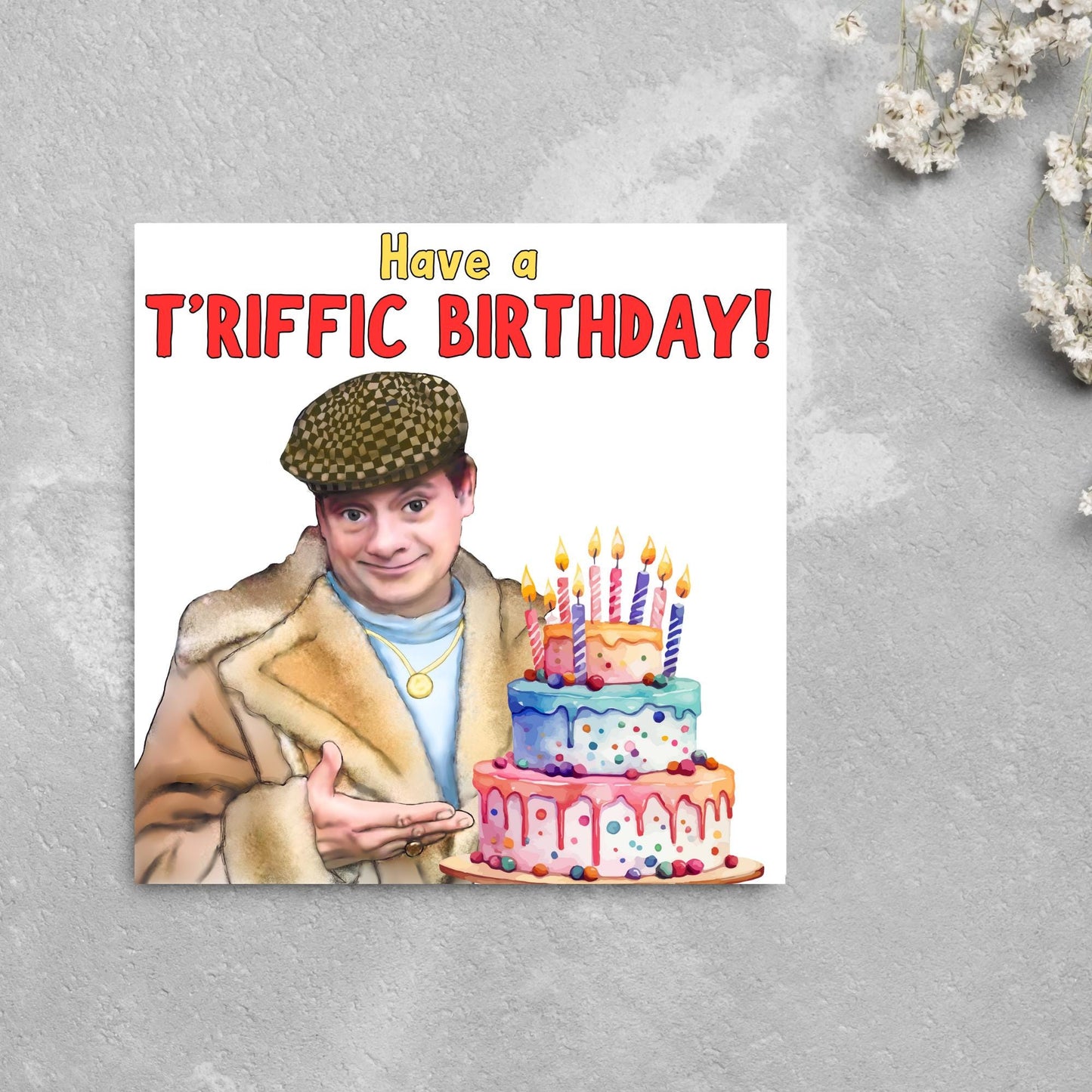 This square shaped card has an illustration of Del Boy from the British Sitcom Only Fools and Horses. The Card has Del Boy standing and pointing at an illustration of a triple tower birthday cake. The Caption reads have a T'riffic Birthday! The Caption is in a mustard yellow and ketchup red