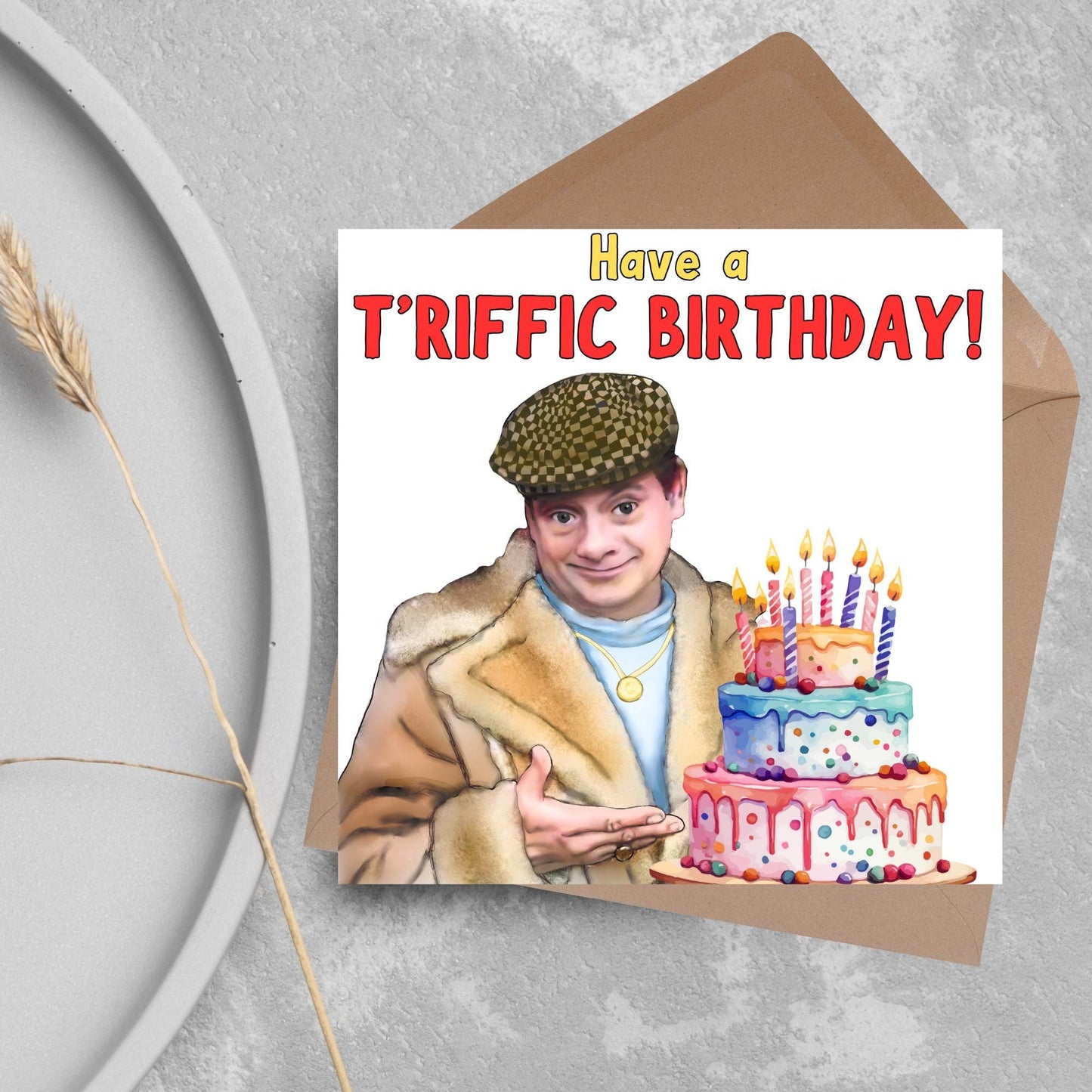 This square shaped card has an illustration of Del Boy from the British Sitcom Only Fools and Horses. The Card has Del Boy standing and pointing at an illustration of a triple tower birthday cake. The Caption reads have a T'riffic Birthday! The Caption is in a mustard yellow and ketchup red