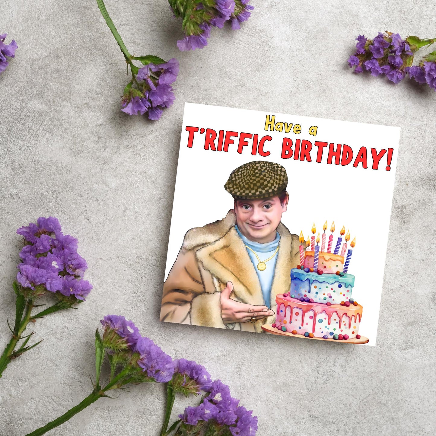This square shaped card has an illustration of Del Boy from the British Sitcom Only Fools and Horses. The Card has Del Boy standing and pointing at an illustration of a triple tower birthday cake. The Caption reads have a T'riffic Birthday! The Caption is in a mustard yellow and ketchup red