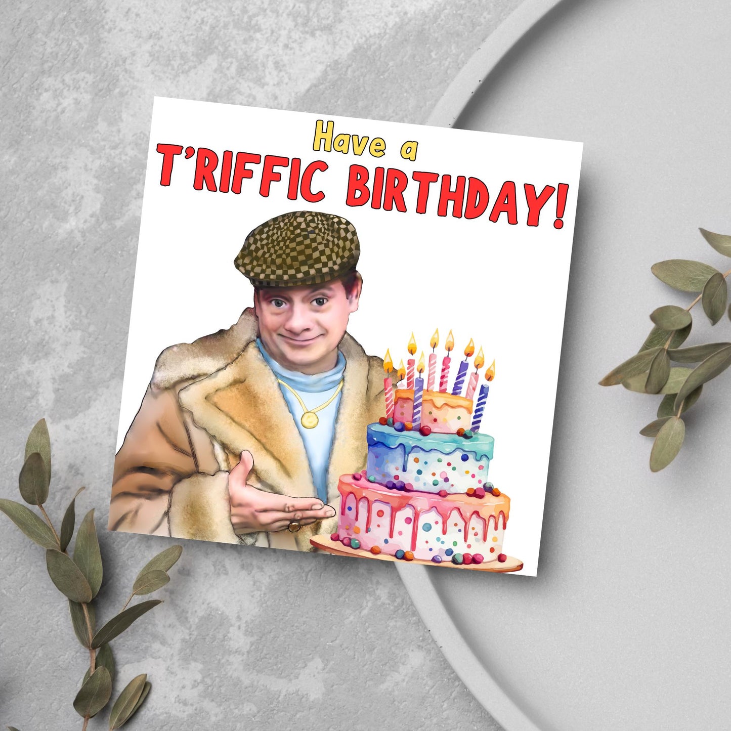This square shaped card has an illustration of Del Boy from the British Sitcom Only Fools and Horses. The Card has Del Boy standing and pointing at an illustration of a triple tower birthday cake. The Caption reads have a T'riffic Birthday! The Caption is in a mustard yellow and ketchup red