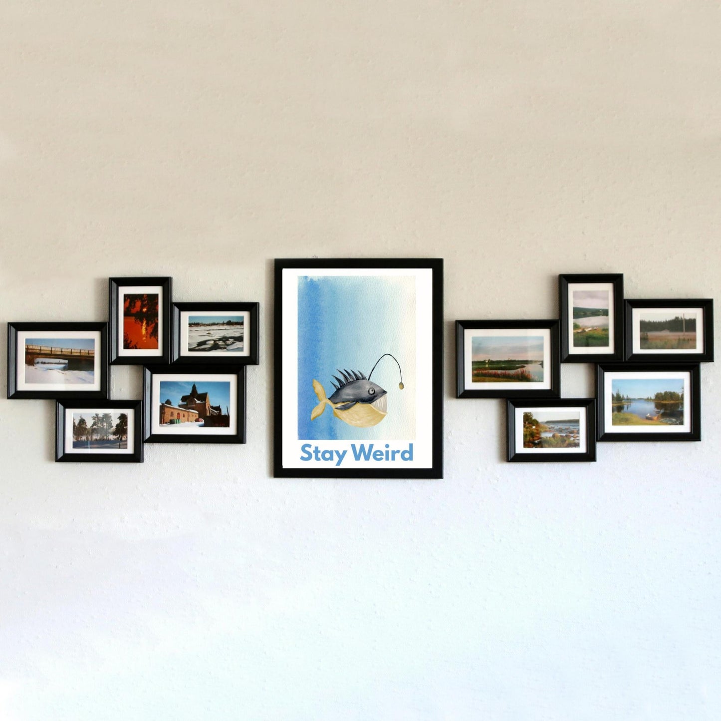 A framed A4 art print featuring a whimsical watercolor illustration of an anglerfish with a yellow tail and light lure, set against a blue gradient background. Below the fish, bold blue text reads "Stay Weird."