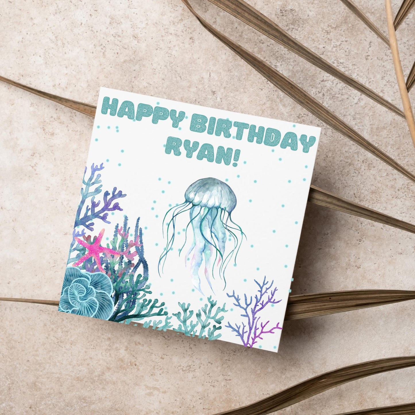 Image of a square Birthday card. Card has a white background and a watercolour style jellyfish amongst coral and seaweed. All the colours are blues, greens, pinks and purples. At the top of the card is bold blue text that says happy birthday ryan which can be personalised to any name.