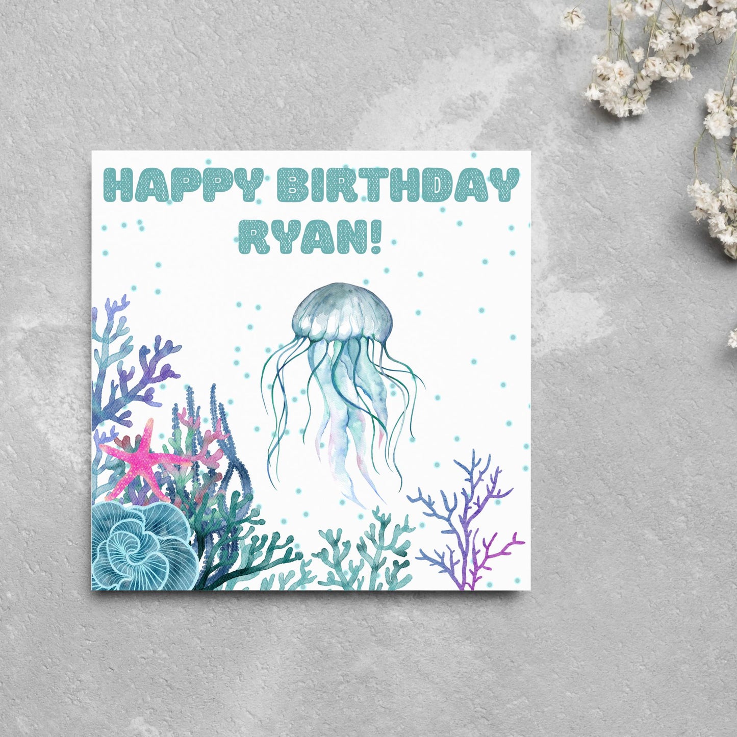 Image of a square Birthday card. Card has a white background and a watercolour style jellyfish amongst coral and seaweed. All the colours are blues, greens, pinks and purples. At the top of the card is bold blue text that says happy birthday ryan which can be personalised to any name.