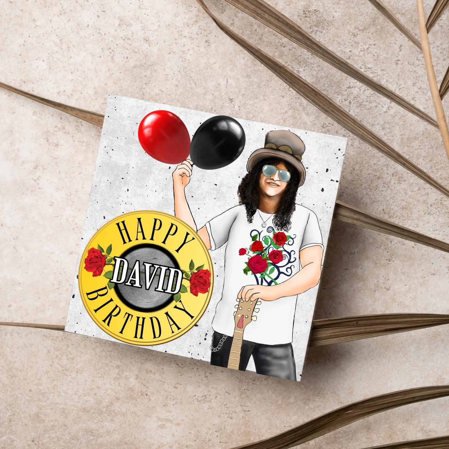 Square Birthday card with an illustration of Slash from Guns and Roses holding a red balloon and a black balloon in one hand, and resting his other on his guitar. He is wearing his trademark top hat, a rose print tee shirt and sunglasses. There is a band style logo that reads happy birthday david to the left of him.