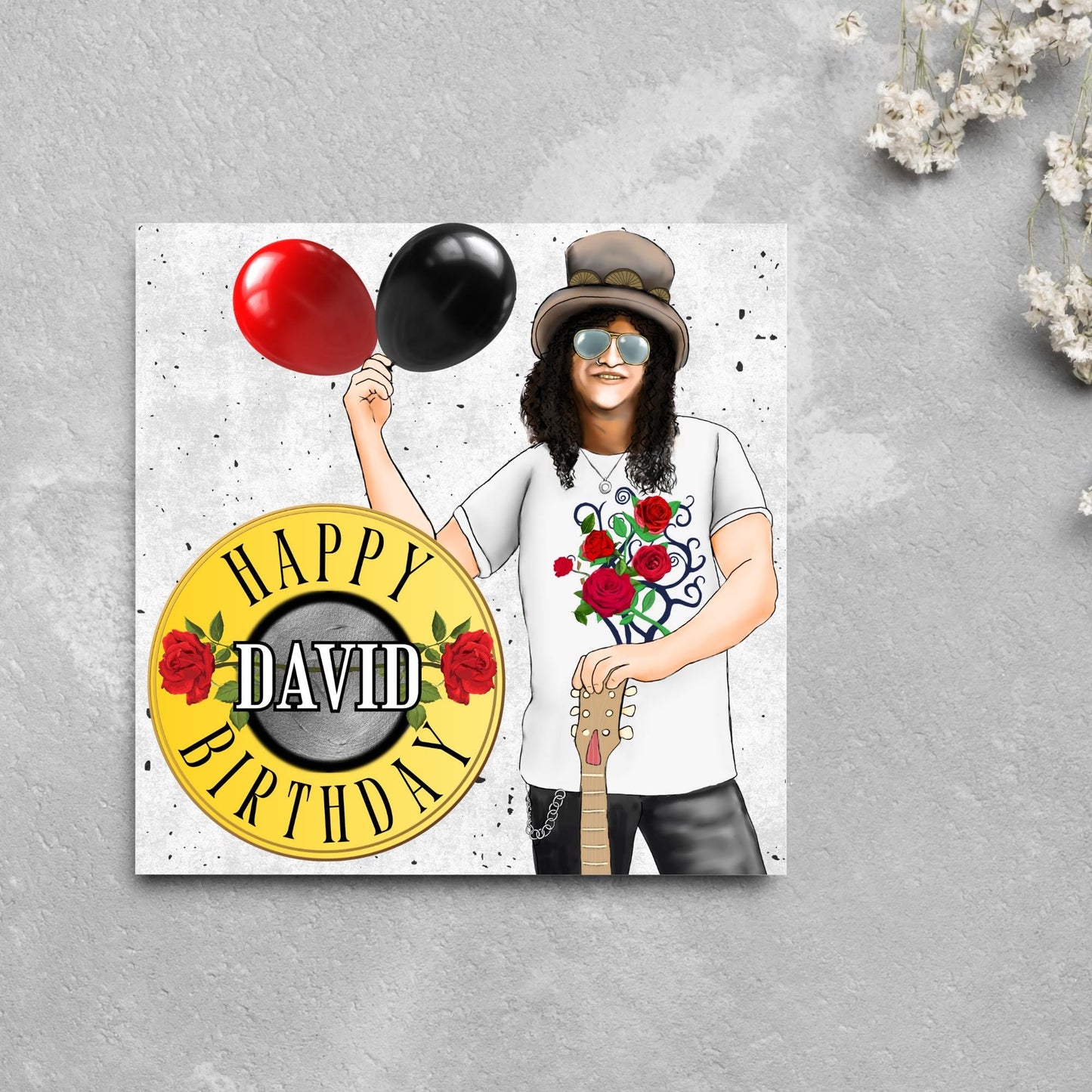 Square Birthday card with an illustration of Slash from Guns and Roses holding a red balloon and a black balloon in one hand, and resting his other on his guitar. He is wearing his trademark top hat, a rose print tee shirt and sunglasses. There is a band style logo that reads happy birthday david to the left of him.