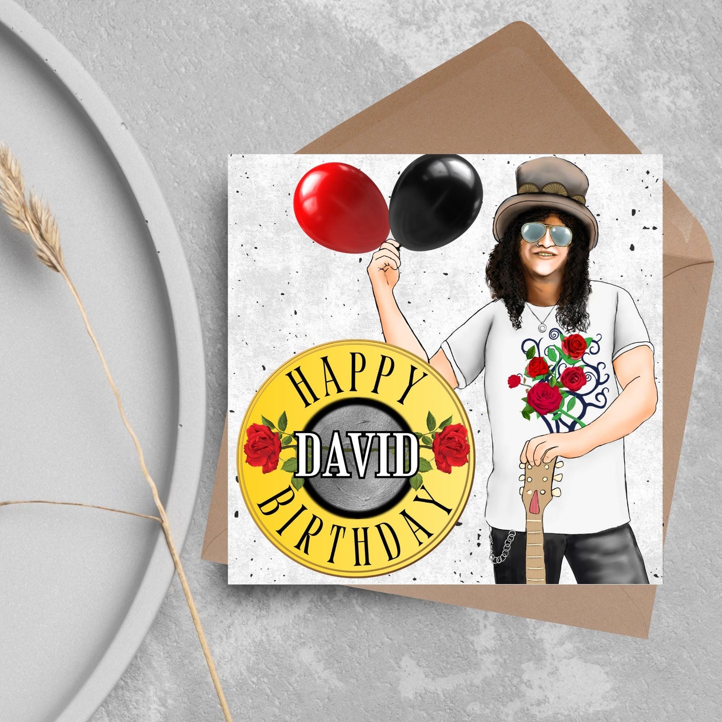 Square Birthday card with an illustration of Slash from Guns and Roses holding a red balloon and a black balloon in one hand, and resting his other on his guitar. He is wearing his trademark top hat, a rose print tee shirt and sunglasses. There is a band style logo that reads happy birthday david to the left of him.
