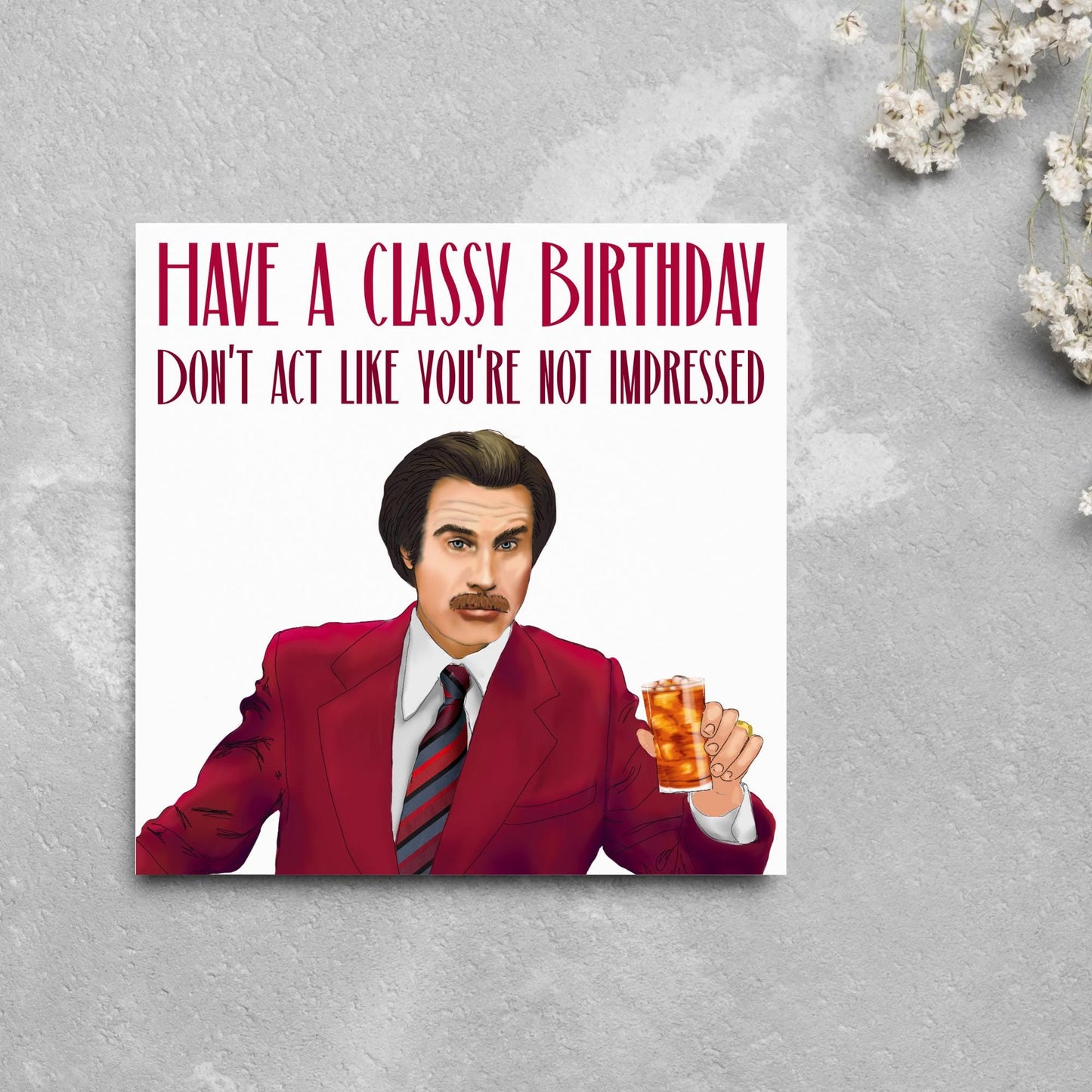 image of a square birthday card, the card has a white background with a hand drawn illustration of Ron Burgandy from the Movie Anchorman in a dark red suit holding a glass of whiskey. Above him is dark red capitalised text that reads 'Have a classy birthday, Don't act like you're not impressed.'