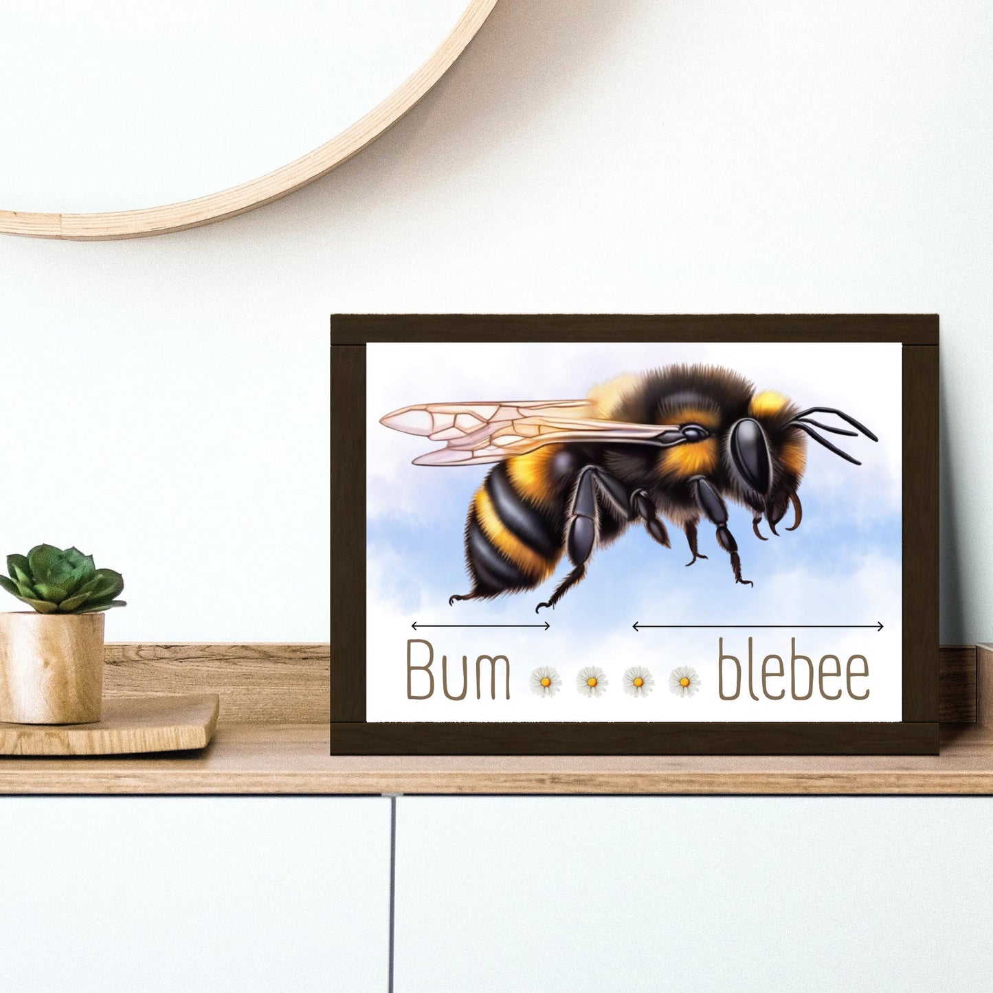 A framed A4 art print featuring a detailed illustration of a bumblebee with soft blue sky in the background. Below the bee, the text playfully reads "Bum" followed by five daisy icons and then "blebee," with arrows pointing across the entire phrase to emphasise the humorous, stretched-out pun