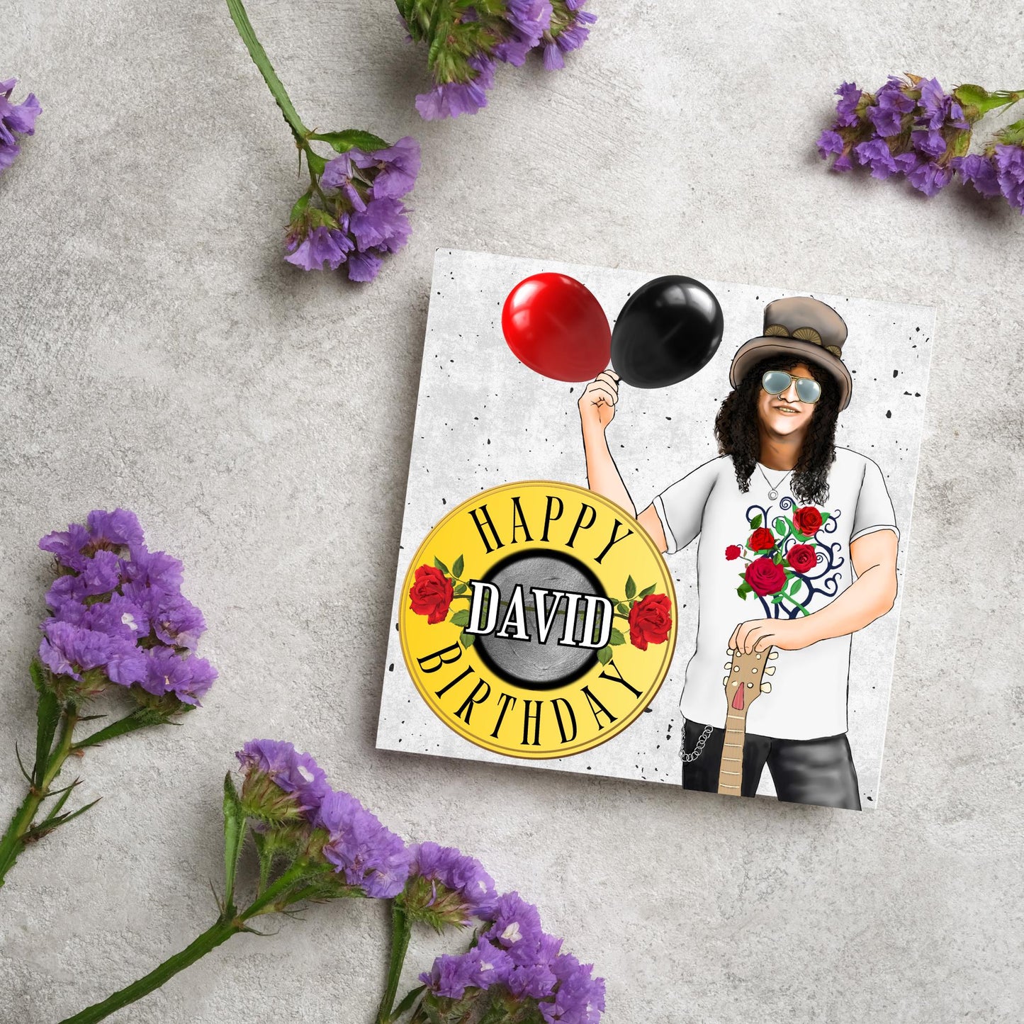 Square Birthday card with an illustration of Slash from Guns and Roses holding a red balloon and a black balloon in one hand, and resting his other on his guitar. He is wearing his trademark top hat, a rose print tee shirt and sunglasses. There is a band style logo that reads happy birthday david to the left of him.