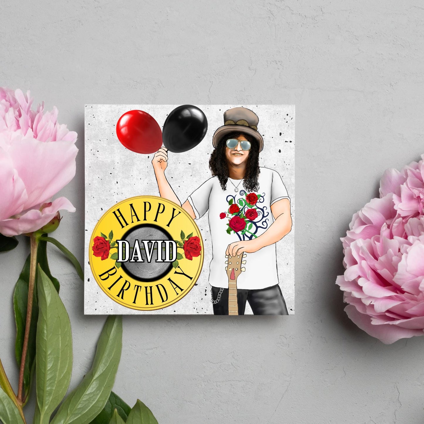 Square Birthday card with an illustration of Slash from Guns and Roses holding a red balloon and a black balloon in one hand, and resting his other on his guitar. He is wearing his trademark top hat, a rose print tee shirt and sunglasses. There is a band style logo that reads happy birthday david to the left of him.