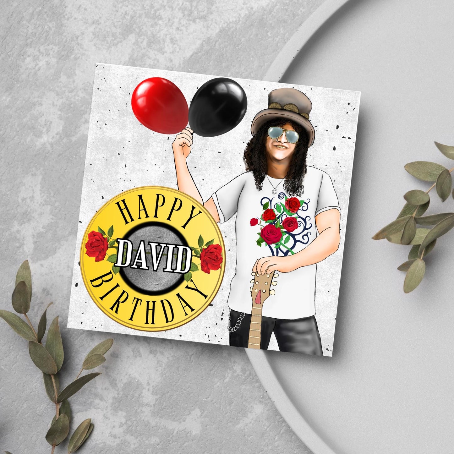 Square Birthday card with an illustration of Slash from Guns and Roses holding a red balloon and a black balloon in one hand, and resting his other on his guitar. He is wearing his trademark top hat, a rose print tee shirt and sunglasses. There is a band style logo that reads happy birthday david to the left of him.