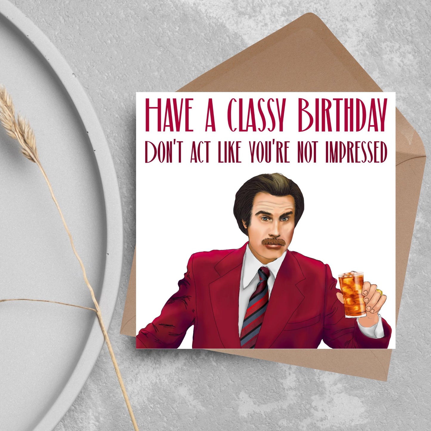 image of a square birthday card, the card has a white background with a hand drawn illustration of Ron Burgandy from the Movie Anchorman in a dark red suit holding a glass of whiskey. Above him is dark red capitalised text that reads 'Have a classy birthday, Don't act like you're not impressed.'