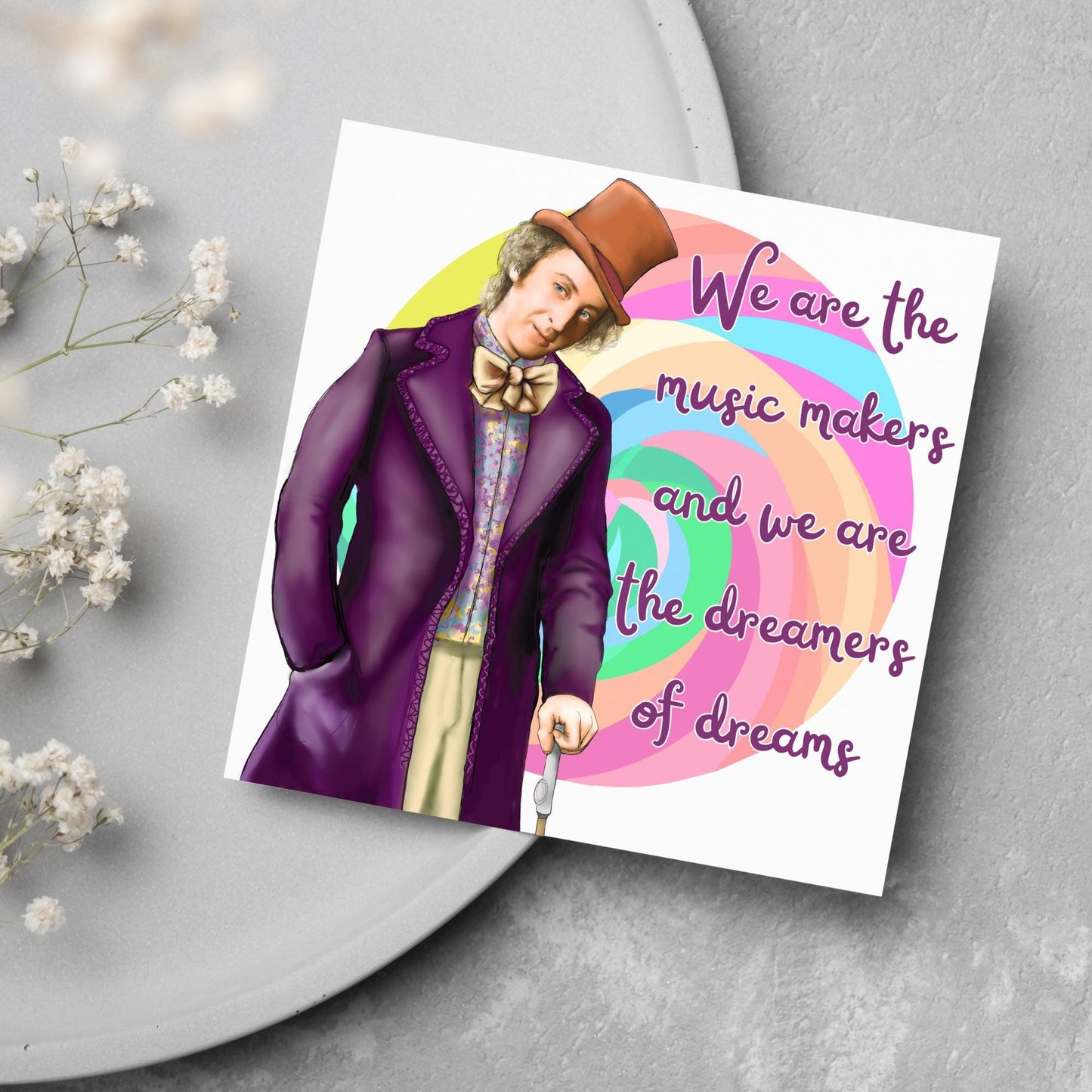 Image of a square greeting card. The background of the card is white and there is a hand drawn image of Gene Wilder as Willy Wonka wearing his purple coat, top hat and bow tie. Behind him is a colourful swirly lollypop and purple text reads 'we are the music makers and we are the dreamers of dreams' in a curly font.