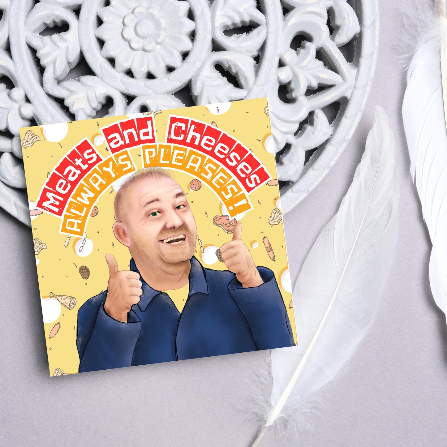 Square greeting card with a hand drawn image of Bob MOrtimer with 2 thumbs up against a backdrop of swiss cheese and various illustrations of different types of meat, with arched text that reads 'meats and cheeses always pleases'