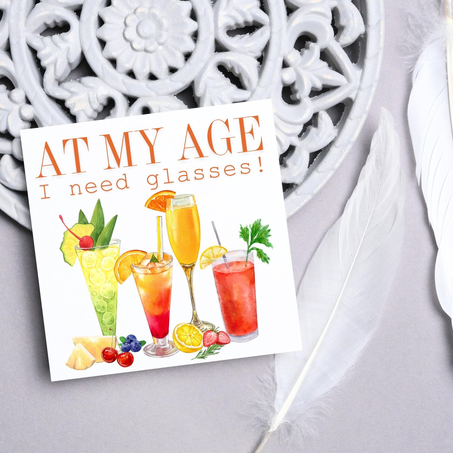Image of a square birthday card with colourful illustrations of cocktails with the text - at my age I need glasses!