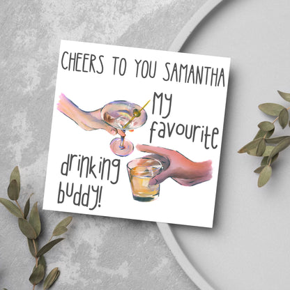 Square card with watercolour design of 2 hands holding drinks glasses against a white background, with grey text that reads &quot;cheers to you Samantha, my favourite drinking buddy&quot;