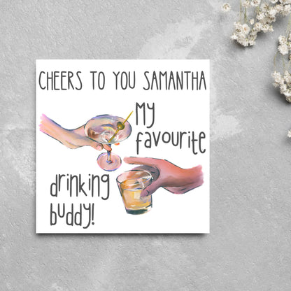 Square card with watercolour design of 2 hands holding drinks glasses against a white background, with grey text that reads &quot;cheers to you Samantha, my favourite drinking buddy&quot;
