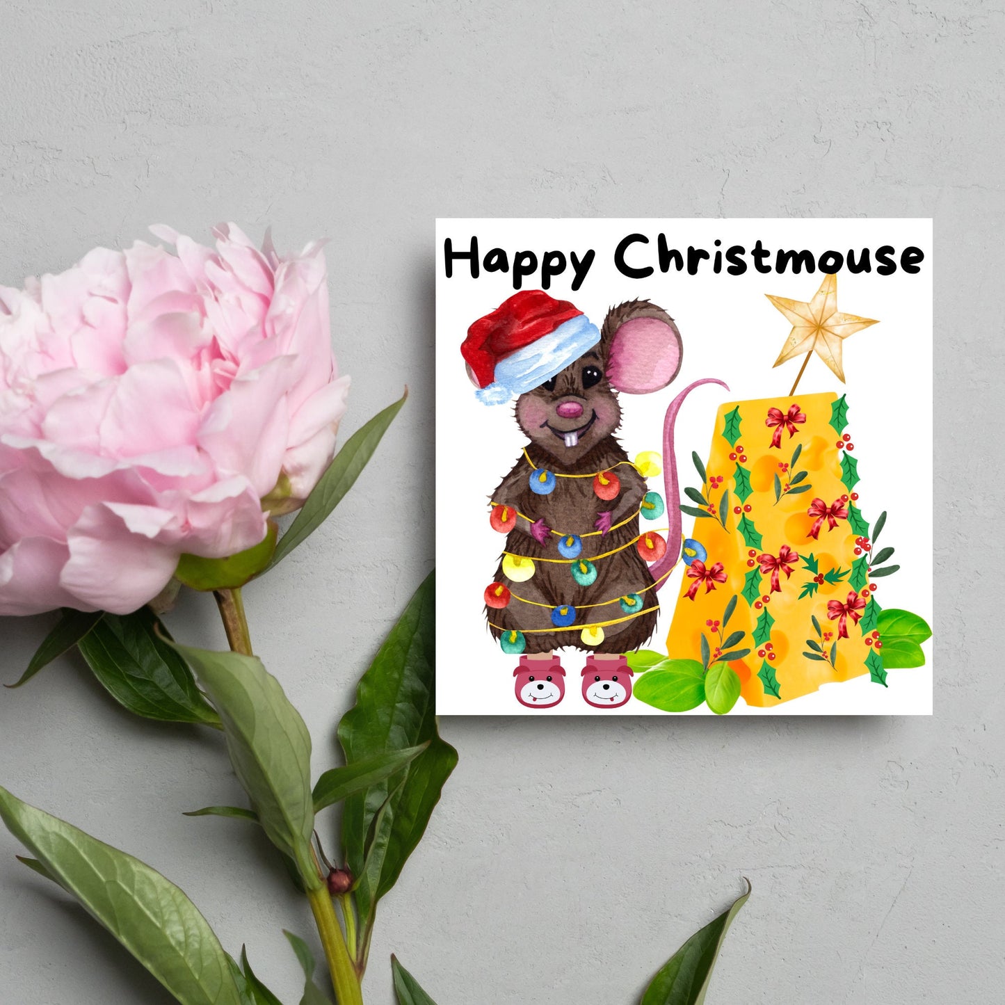 Square Christmas card featuring a cartoon mouse wrapped in christmas lights and wearing a santa hat and slippers next to a christmas tree made from cheese with decorations of holly and red bows. The text, Happy Christmouse is written at the top