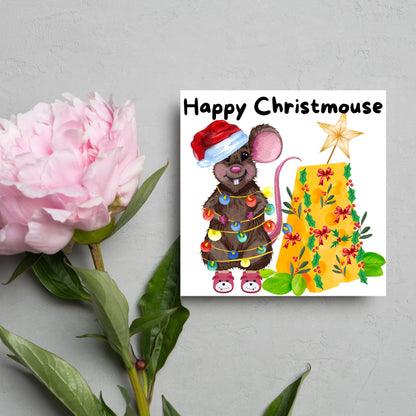 Square Christmas card featuring a cartoon mouse wrapped in christmas lights and wearing a santa hat and slippers next to a christmas tree made from cheese with decorations of holly and red bows. The text, Happy Christmouse is written at the top