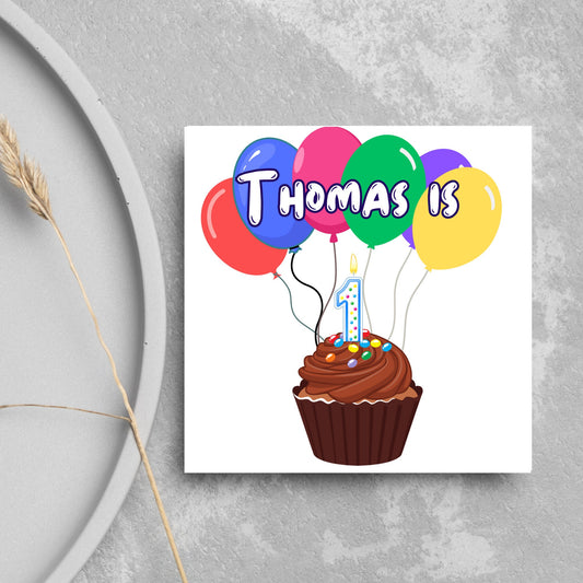 square childs birthday card with chocolate cupcake design personalised with name balloons and a number 1 candle. card reads thomas is 1