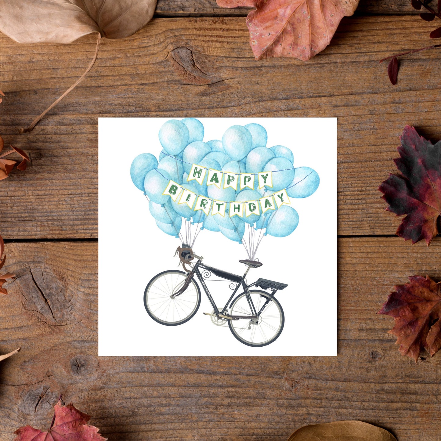White square birthday card with an illustration of a bicycle being held aloft by blue watercolour balloons and bunting that reads happy birthday