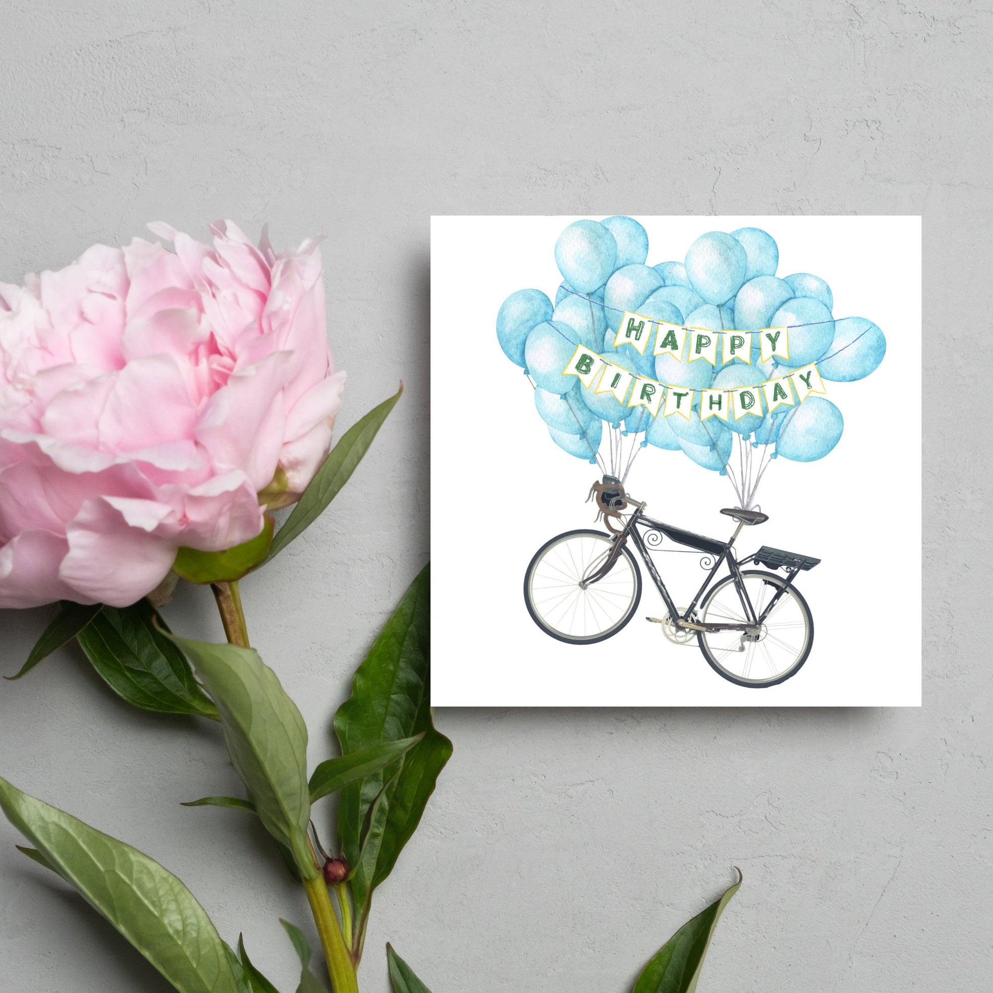 White square birthday card with an illustration of a bicycle being held aloft by blue watercolour balloons and bunting that reads happy birthday