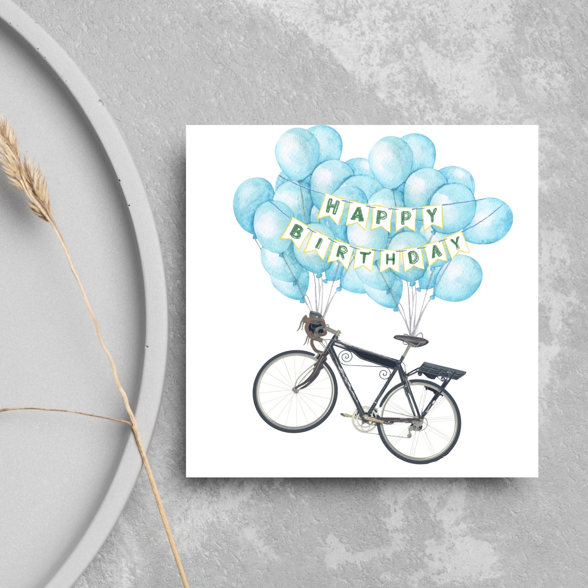White square birthday card with an illustration of a bicycle being held aloft by blue watercolour balloons and bunting that reads happy birthday