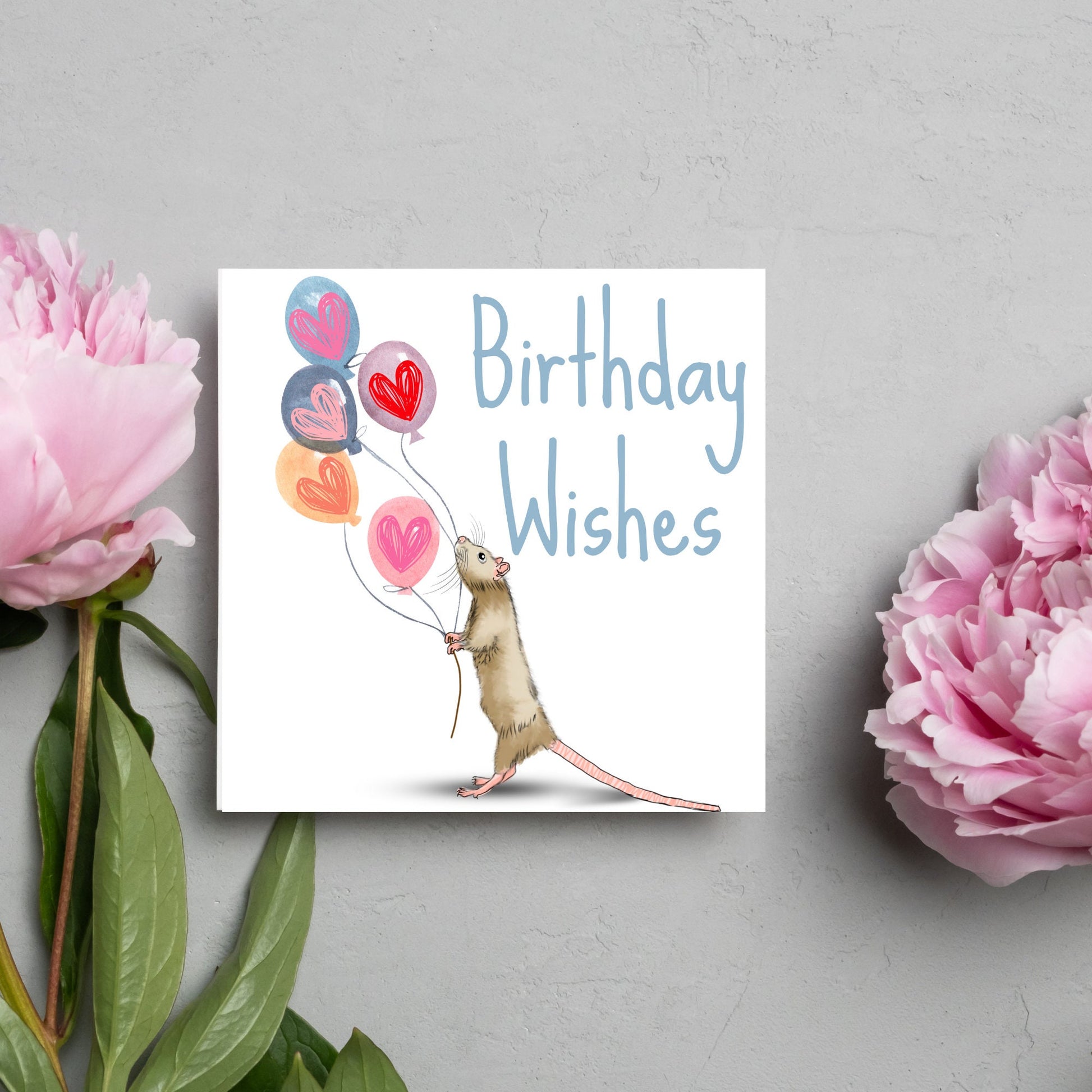 This square card features an illistration of a small mouse/rat holding some balloons with love hearts in a cute cartoon design. The card is captioned Birthday Wishes in a blue handwritten font. The design is on a white background