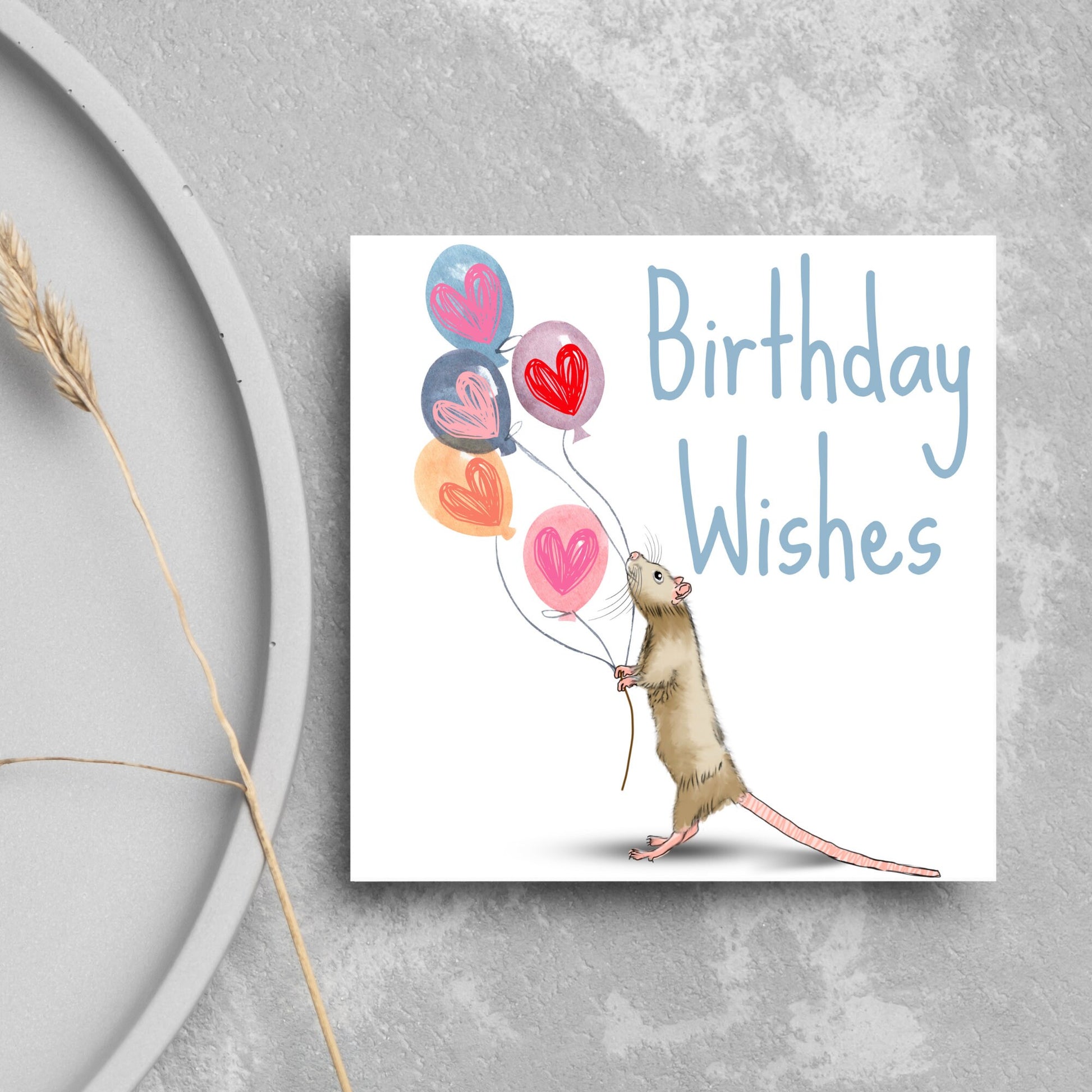 This square card features an illistration of a small mouse/rat holding some balloons with love hearts in a cute cartoon design. The card is captioned Birthday Wishes in a blue handwritten font. The design is on a white background