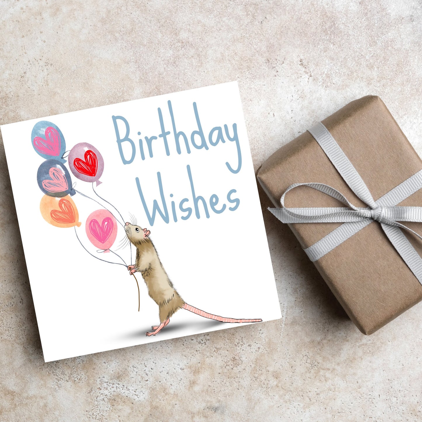 This square card features an illistration of a small mouse/rat holding some balloons with love hearts in a cute cartoon design. The card is captioned Birthday Wishes in a blue handwritten font. The design is on a white background