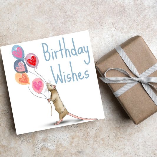 This square card features an illistration of a small mouse/rat holding some balloons with love hearts in a cute cartoon design. The card is captioned Birthday Wishes in a blue handwritten font. The design is on a white background