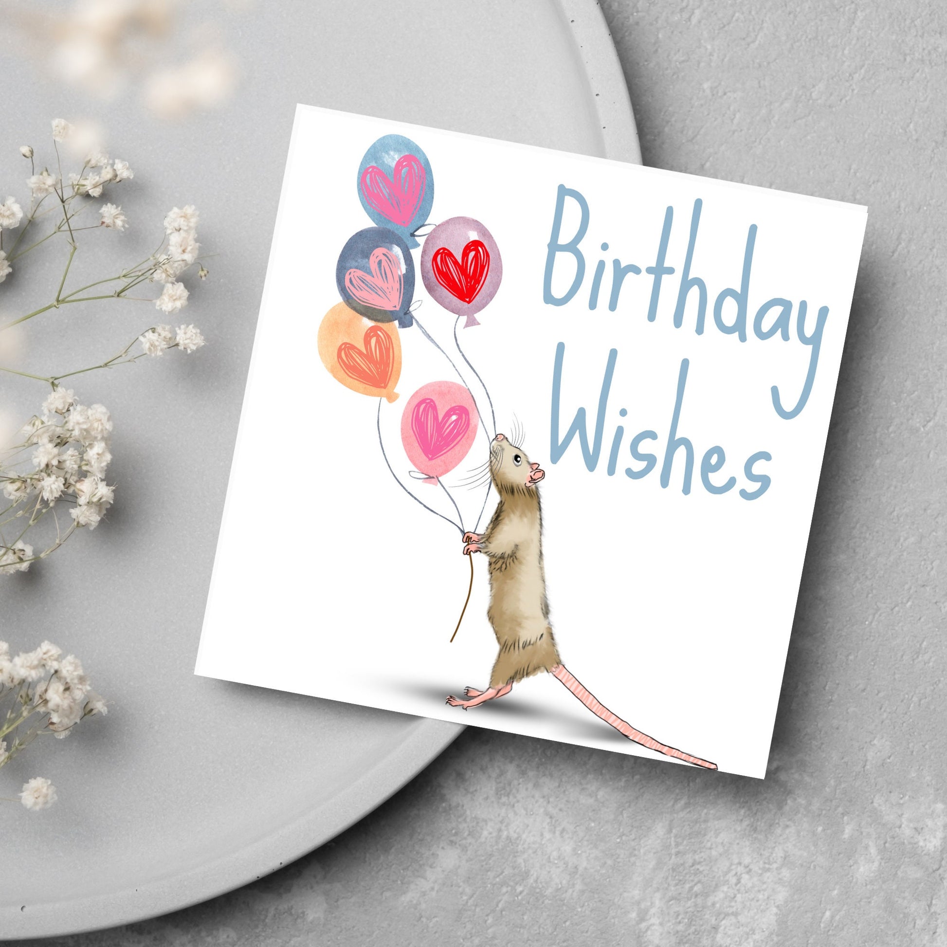 This square card features an illistration of a small mouse/rat holding some balloons with love hearts in a cute cartoon design. The card is captioned Birthday Wishes in a blue handwritten font. The design is on a white background