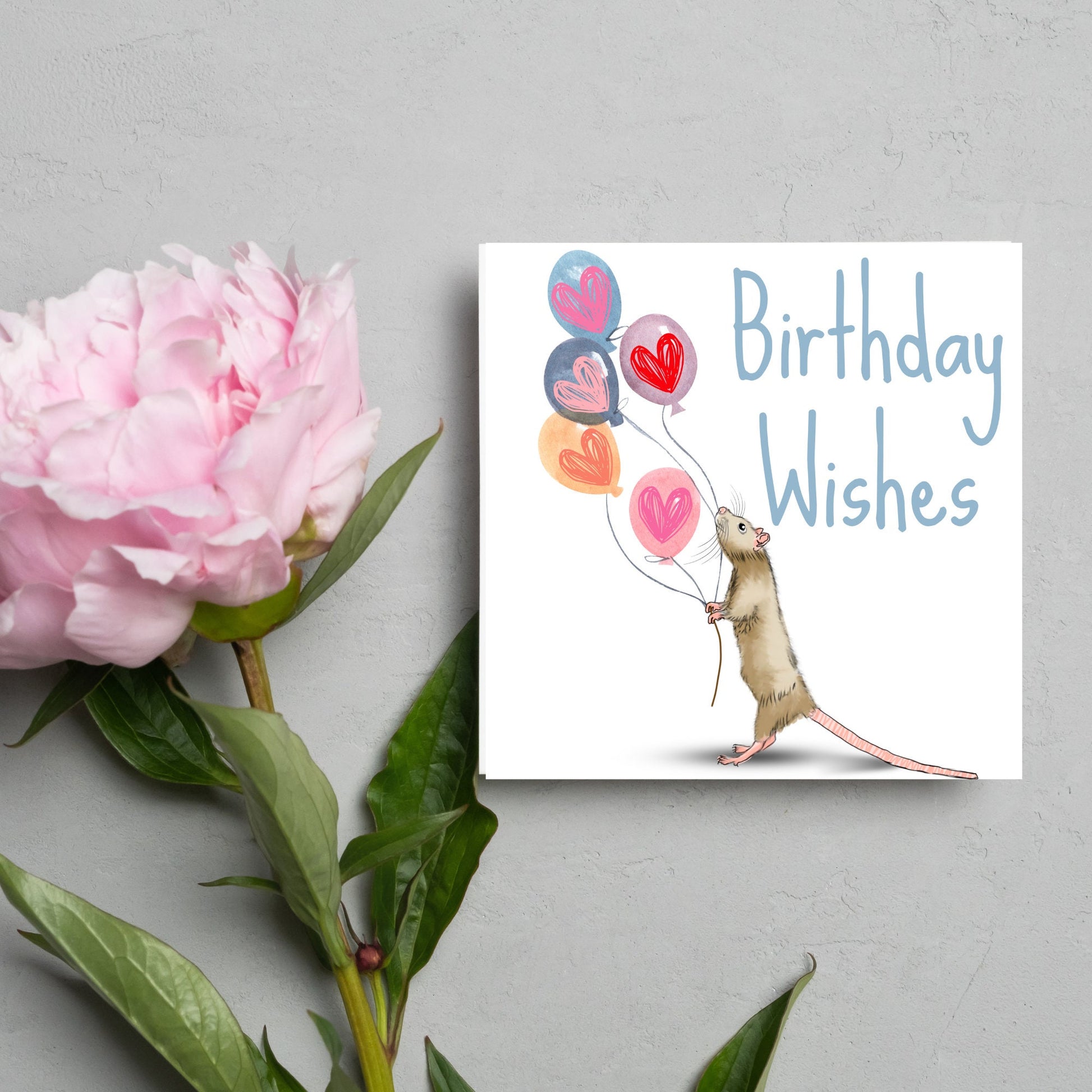 This square card features an illistration of a small mouse/rat holding some balloons with love hearts in a cute cartoon design. The card is captioned Birthday Wishes in a blue handwritten font. The design is on a white background