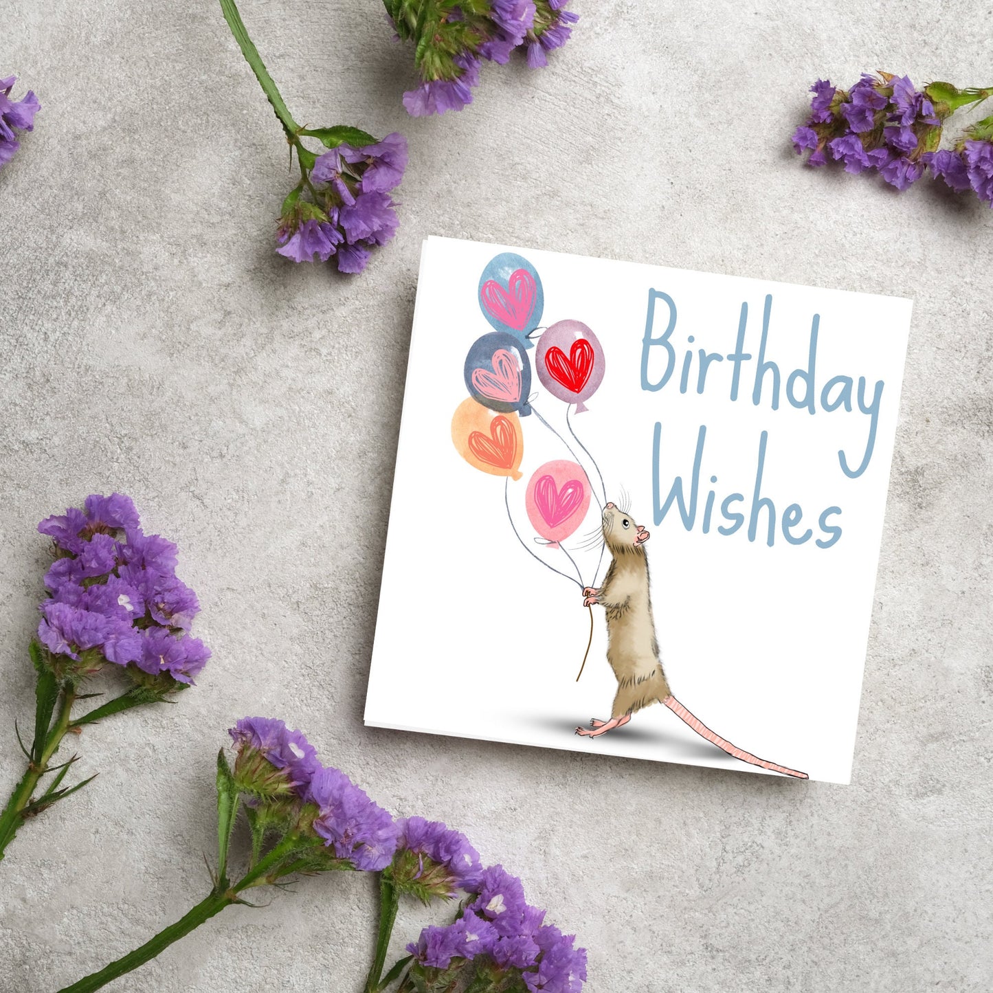 This square card features an illistration of a small mouse/rat holding some balloons with love hearts in a cute cartoon design. The card is captioned Birthday Wishes in a blue handwritten font. The design is on a white background