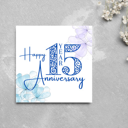 Square Card with white background, there are blue faded watercolour flowers on each corner and dark blue text reads &#39;Happy 15 year anniversary&#39; the words are in a script font and the number is an ornate filigree style