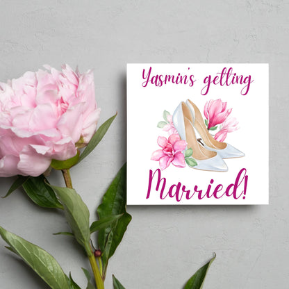 Square card with a watercolour image of white wedding shoes surrounded by pink flowers with pink text that reads Yasmin&#39;s getting married in calligraphy style font