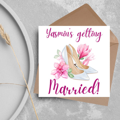 Square card with a watercolour image of white wedding shoes surrounded by pink flowers with pink text that reads Yasmin&#39;s getting married in calligraphy style font
