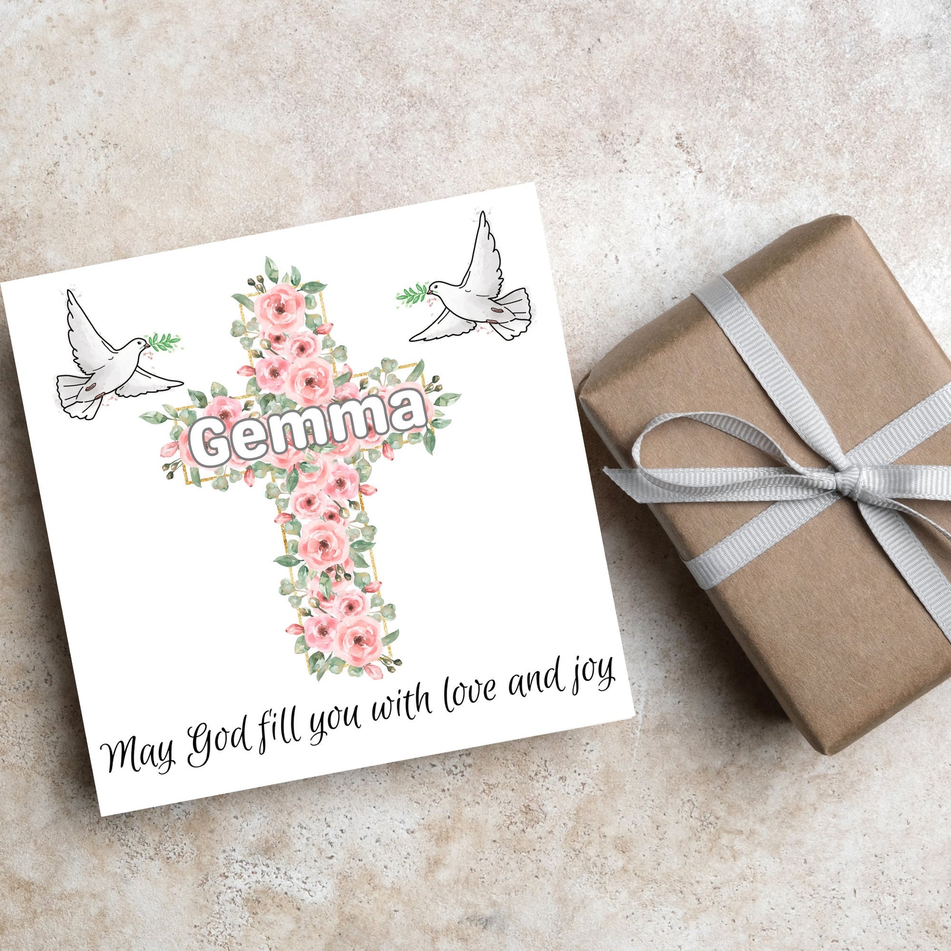 Square white card with a cross made of pink roses at the centre with the chosen name written across in white. either side of the cross is a white dove flying. At the bottom the text &#39;may god fill you with love and joy&#39; is written