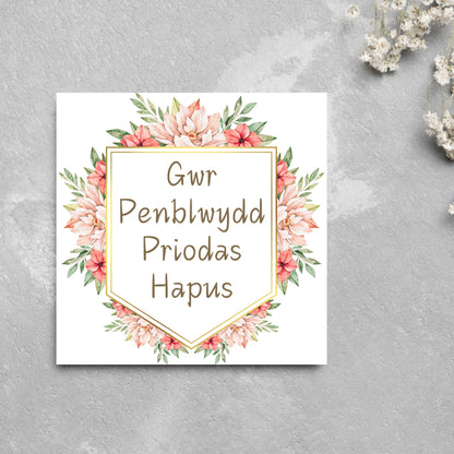 Image of a square wedding anniversary card with &#39;gwr penblwydd priodas hapus&#39; in a subtle handwritten style font, which translates to &#39;happy wedding anniversary&#39; in welsh. the text is against a white banner surrounded by pink flowers